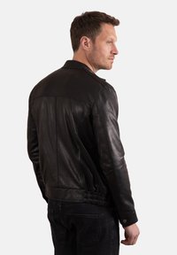 Black leather jacket with a classic design, featuring a standing collar, elasticated hem, and smooth texture. Accentuated by fitted cuffs.