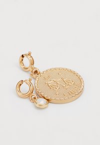 Boucles d'oreilles dorées avec un design de pièce texturée comportant un symbole d'échelle gravé, agrémentées d'un petit cristal rond.