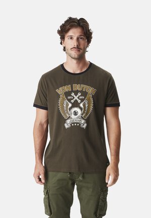 T-shirt vert olive en coton avec col rond, arborant un design graphique avec des ailes et du texte en accents jaune, blanc et noir.