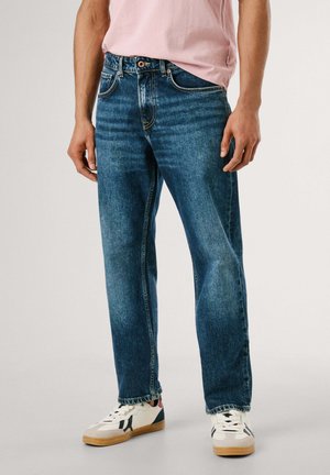 Jeans in denim blu scuro con vestibilità comoda, design a cinque tasche e cuciture a contrasto. Indossati con sneakers bianche con accenti di colore.