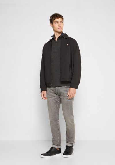 Casaco preto com colarinho, suéter cinza com fecho, jeans cinza claro e ténis pretos com solas brancas. Design simples, sem padrões.