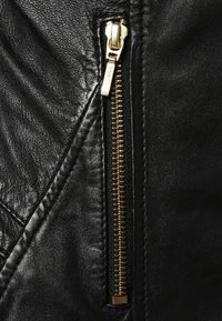 Giacca in pelle nera con zip dorata, finitura texturizzata, dettagli a cucitura inclinata e accenti cuciti lungo i bordi.