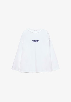 Bela majica z dolgimi rokavi in okroglim izrezom ter temno modrim napisom "PANCAKE ADDICT" na sredini sprednje strani.