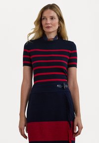 Mornarskoplavi i crveni prugasti pleteni top s rebrastim ovratnikom, kratkim rukavima i glatkom teksturom, uparen s mornarskoplavom suknjom koja ima kontrastni crveni pojas i resice.