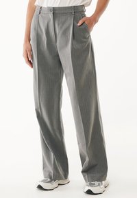 Pantaloni grigi a pieghe realizzati in un tessuto testurizzato, con due tasche laterali e una vita con due bottoni, abbinati a sneaker bianche.