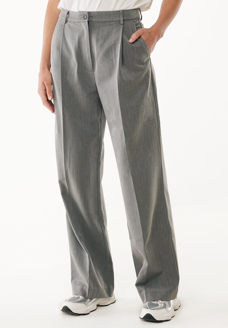 Pantaloni grigi a pieghe realizzati in un tessuto testurizzato, con due tasche laterali e una vita con due bottoni, abbinati a sneaker bianche.