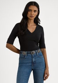 Top preto justo de manga curta com decote em V, combinado com jeans azuis de cintura alta e um cinto prateado decorativo.