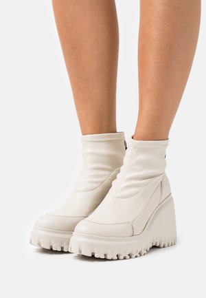 Valkoiset, korkokengät nilkkapituisina, joissa on teksturoitu, nahkaa muistuttava materiaali ja paksut, uritetut pohjat. Ominaisuuksiin kuuluu tyylikäs, tiukka muotoilu.