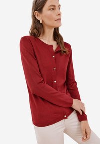 Maglione rosso realizzato in tessuto lavorato a maglia, con collo rotondo, maniche lunghe e chiusura con bottoni sul davanti, dal tocco morbido.