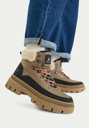 Braune und schwarze Winterstiefel mit dicken Sohlen und Fellfutter, getragen mit hochgekrempelten blauen Jeans und weißen Socken.