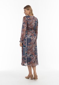 Rochie lungă, cu un model albastru, roșu și alb, cu talie strânsă și mâneci lungi. Realizată dintr-un material ușor, având un design paisley.