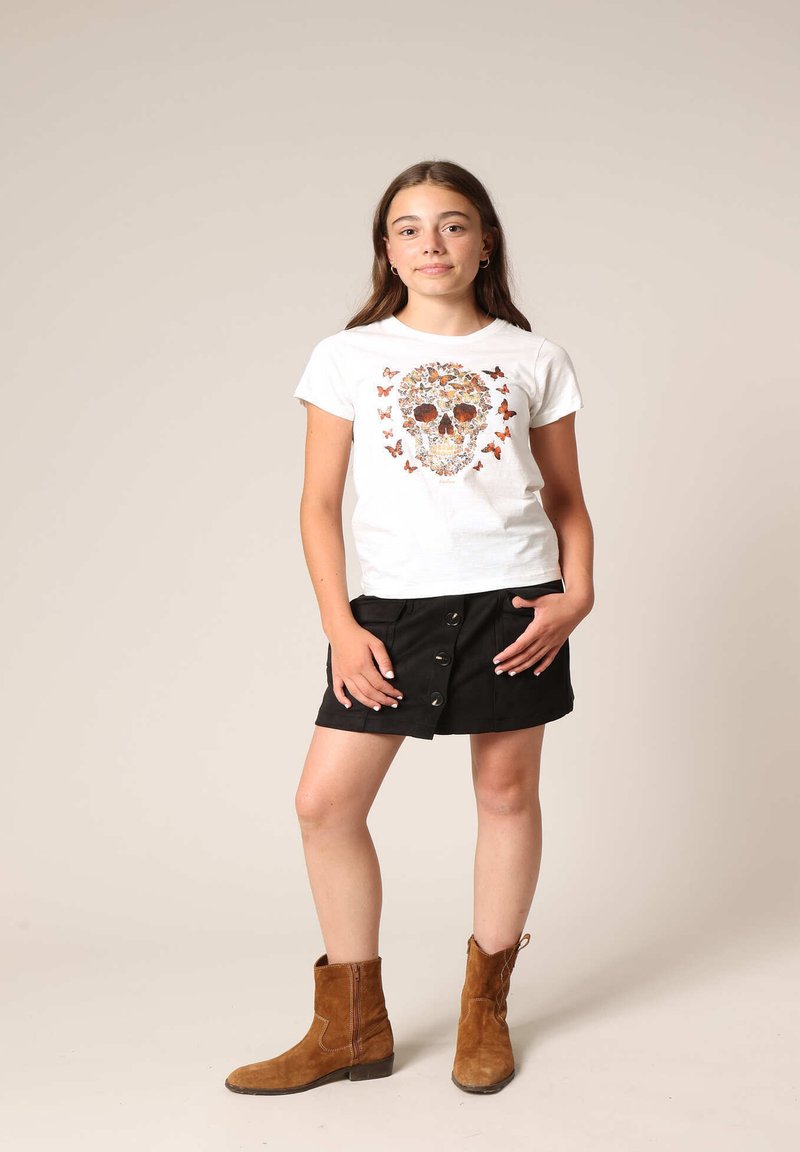 Witte t-shirt met een doodshoofdenontwerp gemaakt van oranje vlinders, gecombineerd met een zwarte rok met knopen, en bruine enkellaarsjes.