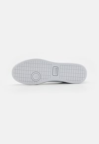 Suola di sneaker bianca con un motivo testurizzato. Presenta un'incisione circolare e il logo del marchio incassato. Finitura liscia e materiale resistente.