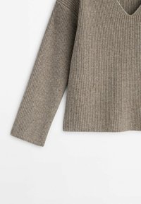 Manche et torse de pull en maille côtelée beige, manches longues et col en V sur fond blanc