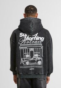 Übergroßer schwarzer Kapuzenpullover mit einem weißen Grafikdruck eines Cafés und eines Autos auf dem Rücken; aus weichem Baumwollstoff gefertigt.