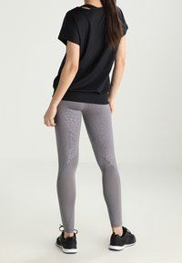 Černý top s krátkými rukávy, volný střih. Šedé legíny s texturovaným vzorem, přiléhavý střih, zužující se nohavice a černé sportovní boty.