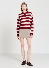 Polo en maille rayé bordeaux et beige avec trois boutons, associé à une mini-jupe beige avec une fente latérale. Des mocassins marron complètent la tenue.