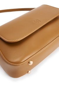 Tan leren schoudertas met klepsluiting, zichtbare stiksels, reliëflogo op de klep en twee gouden metalen studs in de onderste hoek.