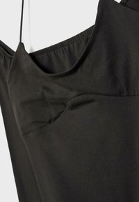 Gros plan sur une robe noire à bretelles spaghetti avec un détail froncé sur le buste et une texture de tissu lisse sur un fond clair.