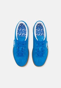 Blauwe suède sneakers met een gestructureerde afwerking, contrasterende witte voering, blauwe veters en een bruine rubberen buitenzool, voorzien van een logolabel.