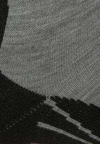 Tejido de punto en negro y gris, con un patrón texturizado que presenta secciones lisas y acanaladas, creando un efecto de degradado.