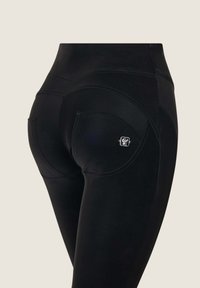 Leggings neri a vita alta realizzati in tessuto elasticizzato, con design a cucitura curva, due tasche posteriori e un piccolo logo accentato sulla tasca.