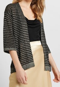 Svart- och vitrandig stickad cardigan med korta ärmar och en texturerad finish, som har en solid svart topp och en satin guldkjol under.