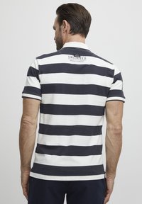 Polo de manga corta con rayas horizontales en azul marino y blanco, un cuello clásico y un logo cerca de la parte posterior del cuello. Material de algodón suave.