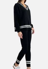 Completo maglione e pantaloni in maglia a trecce neri con dettagli a righe bianche. Design a scollo a V; vestibilità comoda. Il maglione ha maniche lunghe e polsini a costine.
