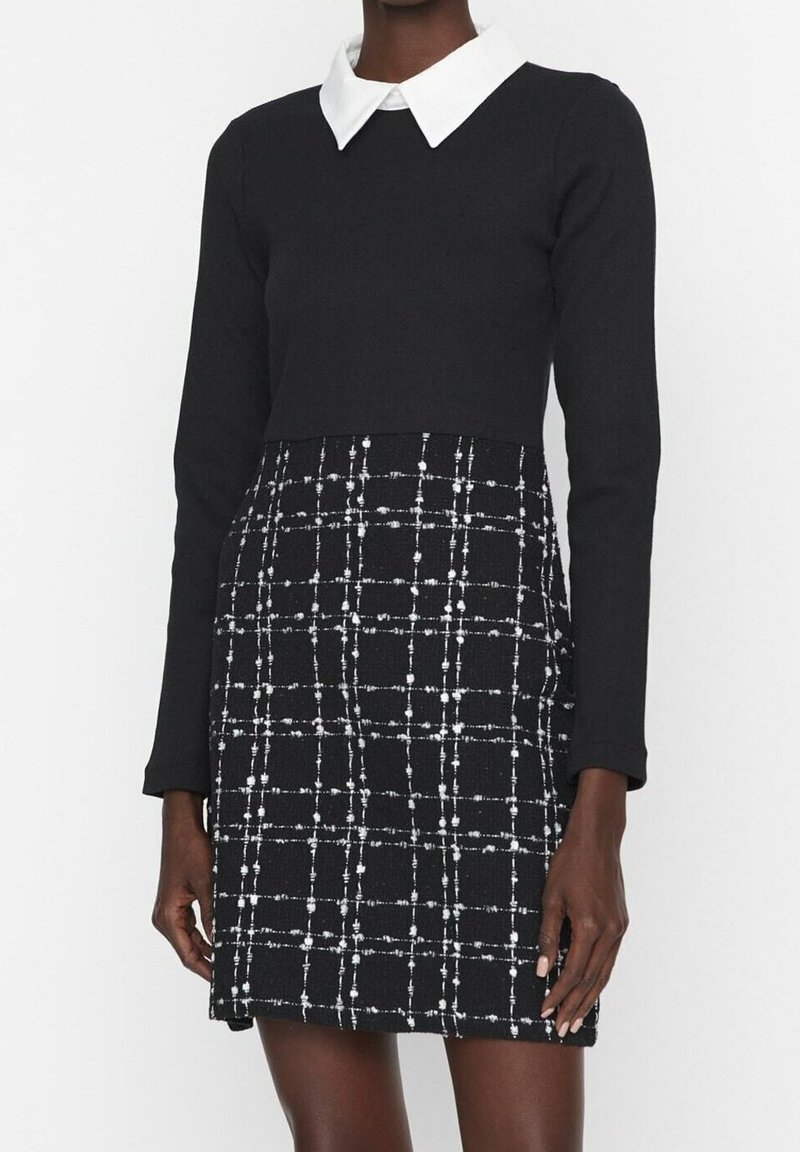 Robe noire à manches longues avec col blanc pointu et partie jupe à carreaux avec lignes blanches croisées et points.