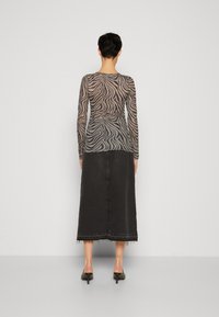 Durchsichtige Langarmbluse mit einem Zebra-Streifenmuster in Grau und Schwarz, kombiniert mit einem hochtaillierten schwarzen Jeansrock mit fransigem Saum.