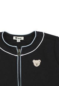 Marineblaue Zip-Jacke mit gerippter Textur, hellblauen Akzenten am Kragen und einem Bärenapplikation auf der linken Brust.