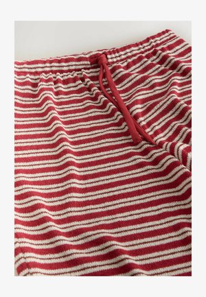 Pantaloni tricotate cu dungi roșii și albe, elastic în talie și șnur roșu pe un fundal alb.