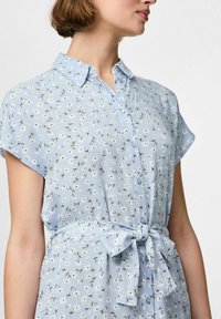 Ljusblå skjortklänning med blommönster, korta ärmar, knäppning framtill och knytbart midjedetalj. Tillverkad av mjukt, lätt material.