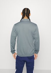 Grå sportsjakke med høj krave og ribbede manchetter, lavet af glat stof. Har en tætsiddende design og minimalistisk stil.