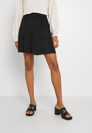 Zwarte suèderen rok met een elastische tailleband, voorzien van twee voorzakken en een vloeiende silhouet, gecombineerd met zwarte sandaalhakken.