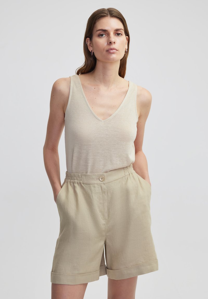 Top sin mangas de color beige claro con escote en V, combinado con pantalones cortos caquis que cuentan con un cierre de botón y dobladillos enrollados, ambos confeccionados en una tela texturizada.