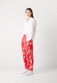 Hvit skjorte med knapper, kremfarget tanktop, røde bukser med blomsterprint og hvite sneakers. Lett materiale med en avslappet passform.