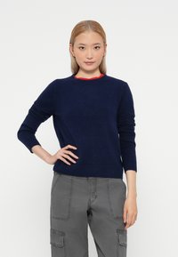 Pulover tricotat albastru marin cu guler rotund și mâneci lungi, având manșete și tiv ribbate, asortat cu pantaloni cargo gri.