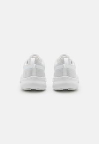 Des chaussures de sport blanches avec une tige en maille, un col rembourré, une languette de tirage et une semelle texturée avec une finition lisse.