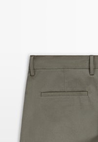 Kaki byxor i ett mjukt tyg, rak midja med bälteshällor och en enda bakficka med en rektangulär klaff.