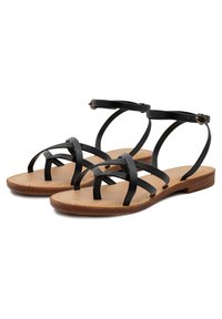 Infradito di pelle nera con più fasce incrociate su una soletta color sabbia e una suola piatta in legno. La cinghia alla caviglia è dotata di una fibbia dorata.