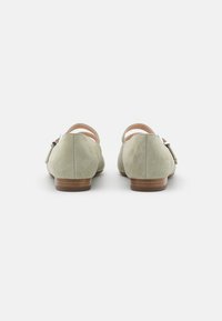 Chaussures en daim vert avec un petit talon, une bride arrière et un détail de boucle décoratif, présentant une texture lisse et une forme arrondie.