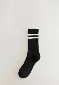 Sort sok med ribbet tekstur, der har en cylindrisk manchet og to vandrette hvide striber øverst.