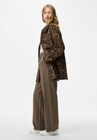 Chaqueta de leopardo de tejido, combinada con pantalones anchos marrones y zapatillas blancas. La chaqueta cuenta con un cuello y un cierre frontal con botones.