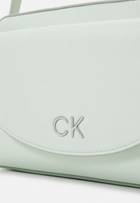 Mintgrön läderaxelväska med silverdetaljer och präglad "CK"-logotyp. Har rundad klaff och texturerad yta.