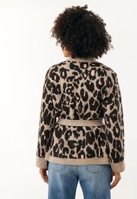 Bruin en beige luipaardprint cardigan met een ceintuur in de taille, gebreide textuur, lange mouwen en een ronde halslijn. Gekleed met blauwe jeans.