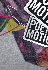 Tela de camiseta gráfica con diseño abstracto multicolor, texto en blanco y negro, y una superficie texturada y brillante.
