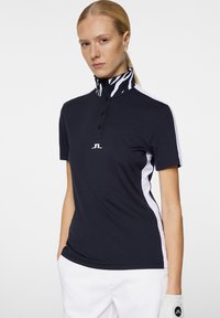 Marinblå pikétröja i ett ventilerande tyg med en krage i svart och vit zebramönster, treknapplåsning och kontrasterande vita sidpaneler.