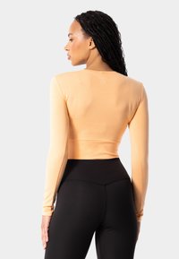 Gaiši oranžs garām piedurknēm apgriezts tops, kas izgatavots no gludas auduma, kopā ar augstām melnām legingām ar bezšuvju dizainu.